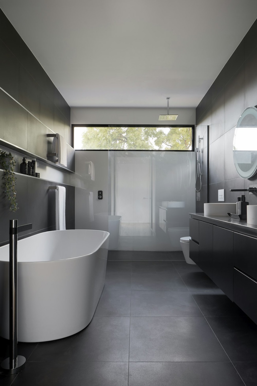 Dark tiled bathroom with a freestanding stone bath and a clerestory window