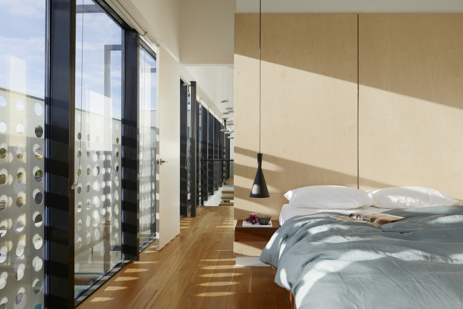 Bedroom with a birch panelled headboard wall and a full height glazed corridor