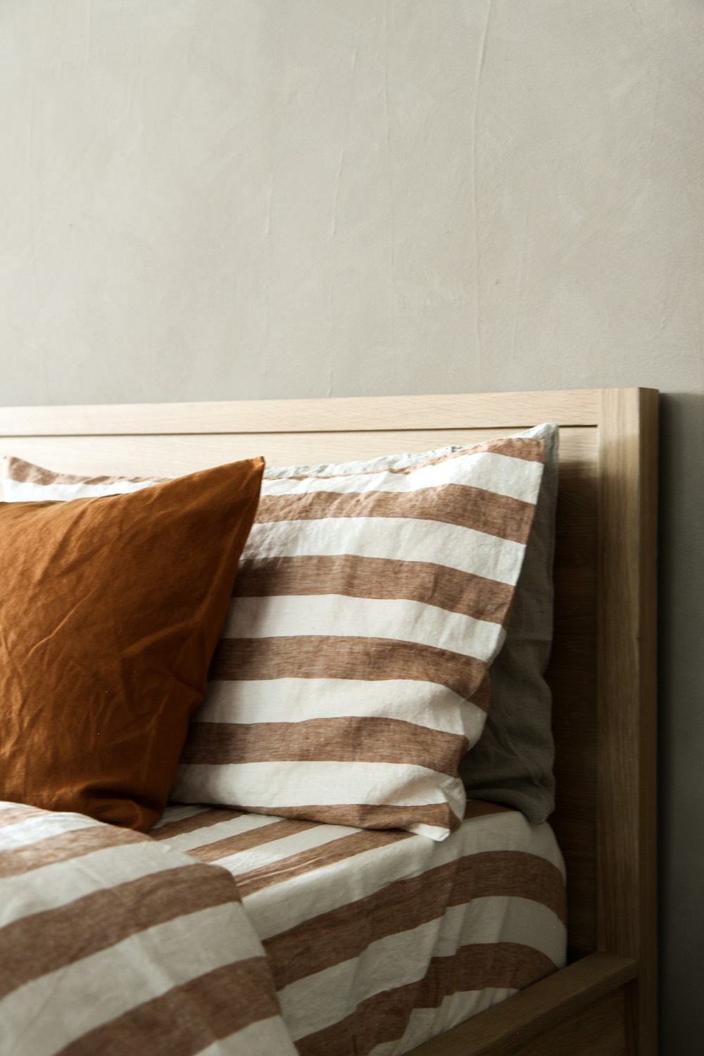 Close view of striped linen bedding against an oak headboard and plaster wall