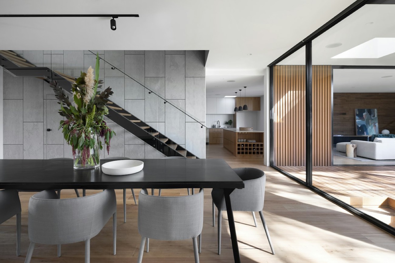 Dining room with a black table, board formed concrete wall and timber screen
