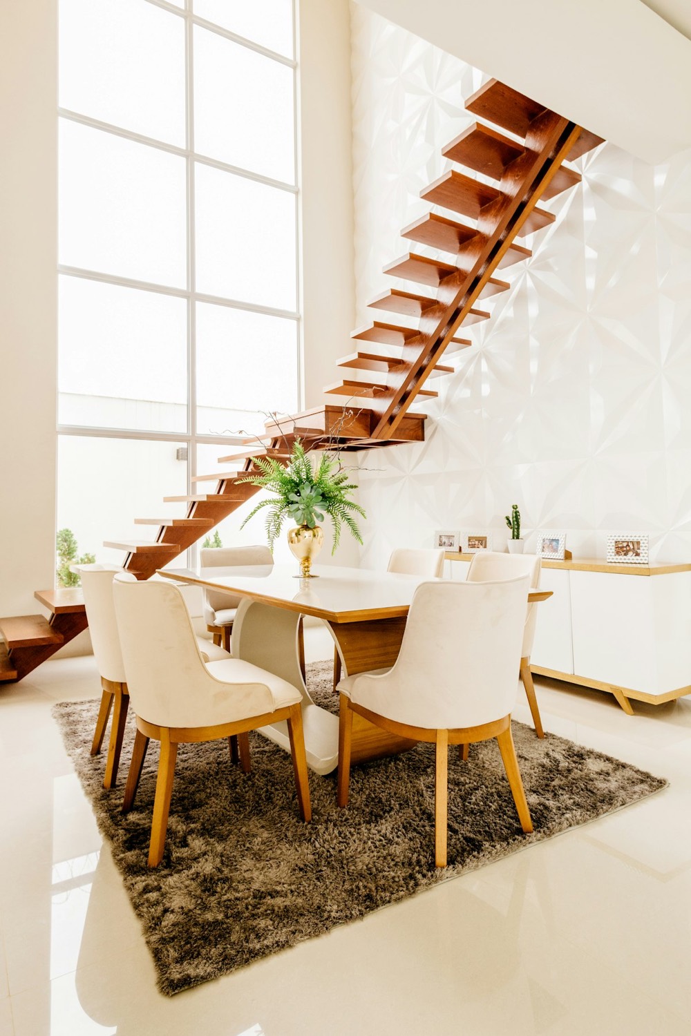 Dining room beneath a sculptural timber staircase and a textured white wall