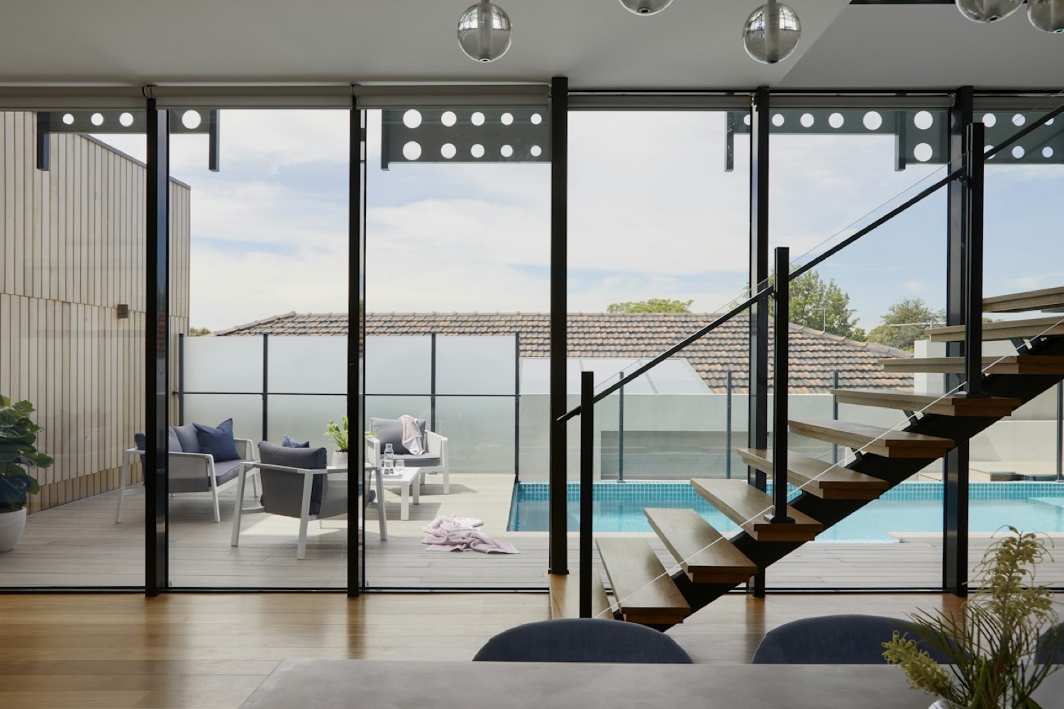 Interior looking through full height glazing to a pool terrace and floating stair